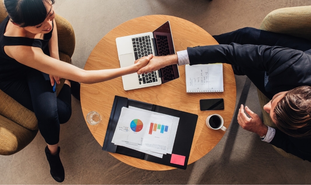 Due persone si stringono la mano sopra un tavolo.