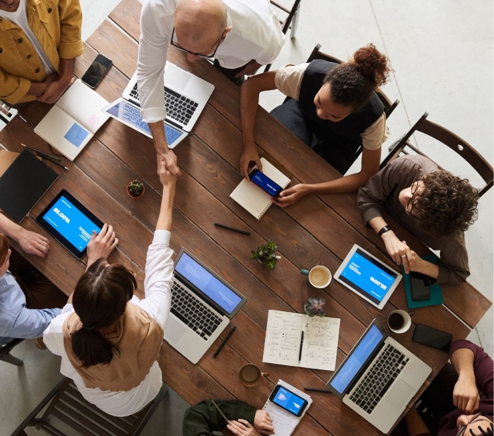 Persone riunite attorno a un tavolo con laptop e tablet.